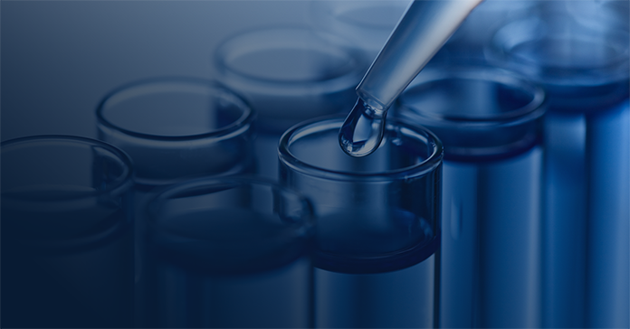 Pipette dropping liquid into clear test tubes in a blue-toned lab setting